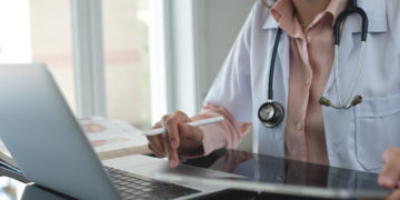 Female doctor working on laptop computer searching the information and using digital tablet at doctor's office. Medical student using computer, healthcare and medicine concept